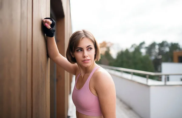 テラスの外に立って休んでいる若いスポーツ女性. — ストック写真