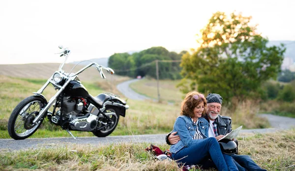 Fröhliches Seniorenpaar mit Karte und Motorrad auf dem Land. — Stockfoto