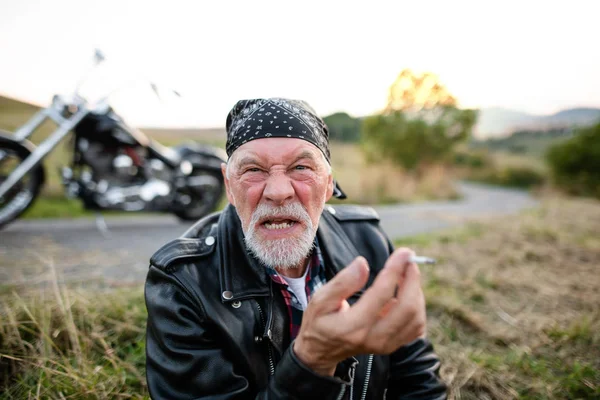 Homme âgé en colère voyageur avec moto dans la campagne, fumer . — Photo