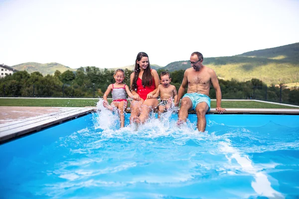 Familia joven con dos niños pequeños sentados junto a la piscina al aire libre . —  Fotos de Stock