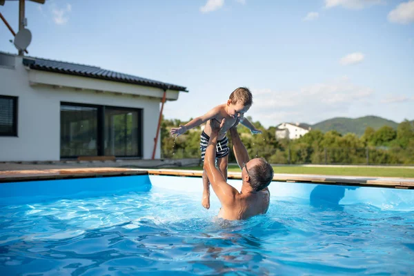 Un padre con un hijo pequeño jugando en la piscina al aire libre . —  Fotos de Stock