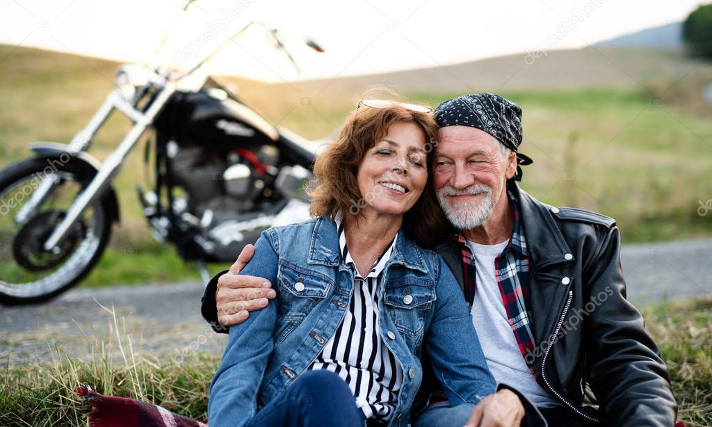 A senior couple travellers with motorbike in countryside, resting.