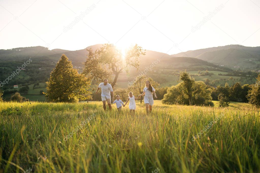 Young family with two small children walking on meadow outdoors at sunset.