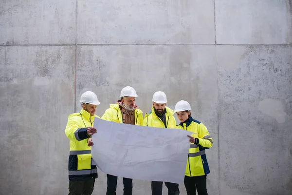 Un gruppo di ingegneri in piedi contro il muro di cemento in cantiere . — Foto Stock