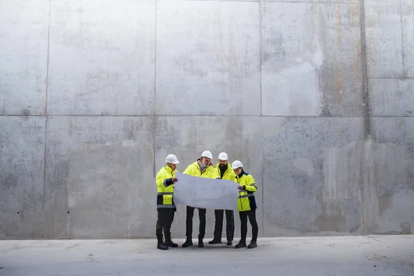 Um grupo de engenheiros de pé contra a parede de concreto no canteiro de obras . — Fotografia de Stock