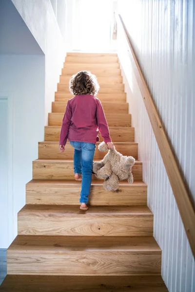 Una vista trasera de una niña pequeña subiendo escaleras de madera en el interior de casa . — Foto de Stock