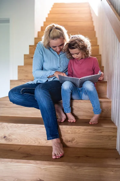 Słodka dziewczynka z matką w domu, czytająca na schodach. — Zdjęcie stockowe
