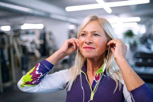 En äldre kvinna med hörlurar i gymmet vilar efter att ha gjort motion. — Stockfoto