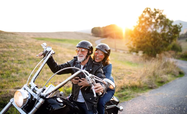 Alegre casal de idosos viajantes com moto no campo ao pôr do sol . — Fotografia de Stock