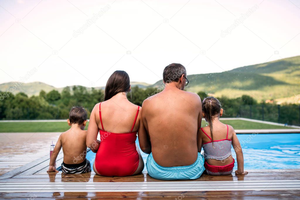 Rear view of family with two small children by swimming pool outdoors.