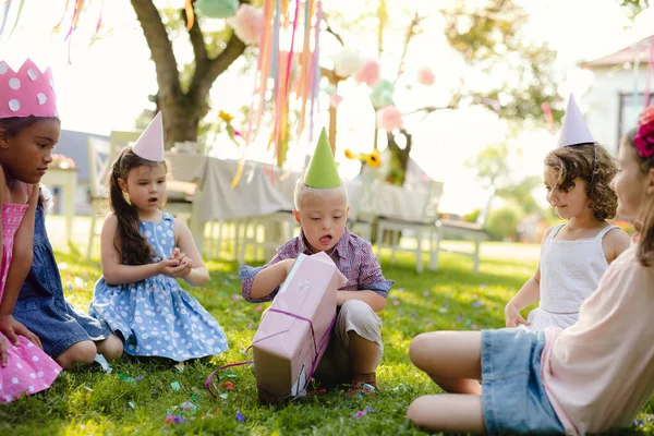 Down sindrome bambino con gli amici sulla festa di compleanno all'aperto, regali di apertura . — Foto Stock