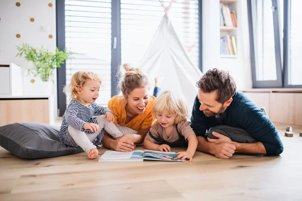 Familia joven con dos niños pequeños en el dormitorio leyendo un libro . — Foto de Stock