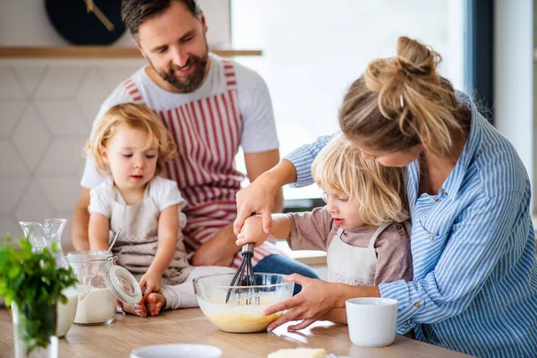 Ung familj med två små barn inomhus i köket, matlagning. — Stockfoto