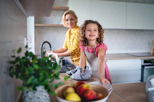 En söt liten flicka med mamma inomhus i köket hemma, diska. — Stockfoto