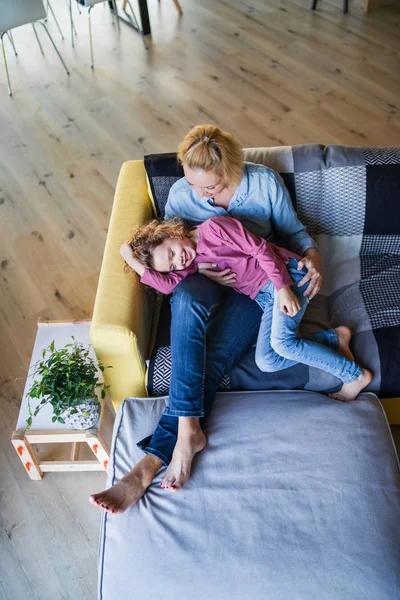 Visão superior da menina pequena bonito com a mãe no sofá em casa, descansando . — Fotografia de Stock