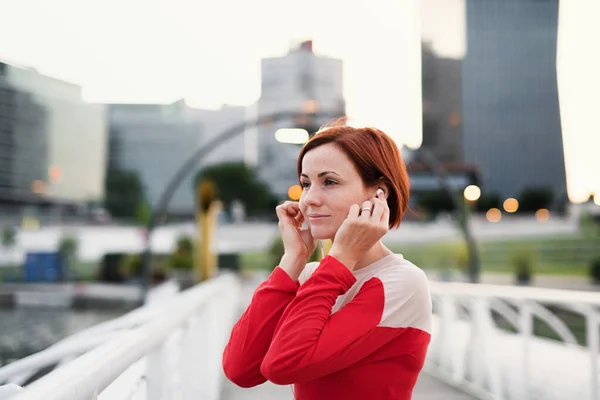 Een jonge vrouw runner met oortjes in de stad, rusten. — Stockfoto