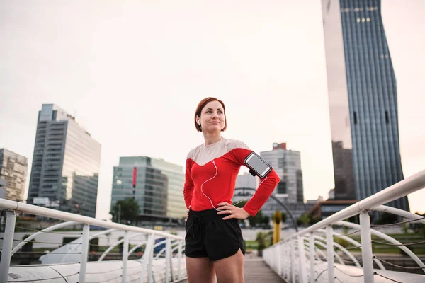 Giovane donna con smartphone in piedi all'aperto in città, a riposo dopo l'esercizio . — Foto Stock