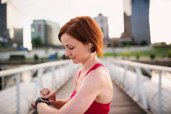 Młoda kobieta ze smartwatchem na moście w mieście, odpoczywa po treningu. — Zdjęcie stockowe