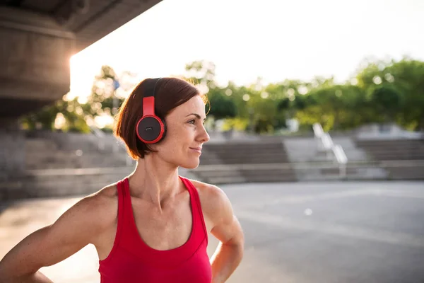 Jovem com fones de ouvido descansando depois de fazer exercício ao ar livre na cidade . — Fotografia de Stock