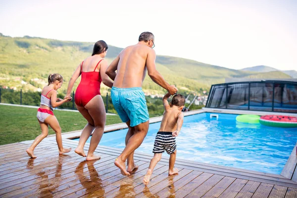 Zadní pohled na rodinu se dvěma malými dětmi u bazénu venku. — Stock fotografie