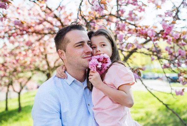 Молодий батько тримає маленьку доньку зовні у весняній природі . — стокове фото