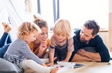 Yatak odasında kitap okuyan iki küçük çocuklu genç bir aile..