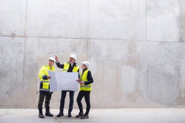 İnşaat alanında beton duvara karşı duran bir grup mühendis..