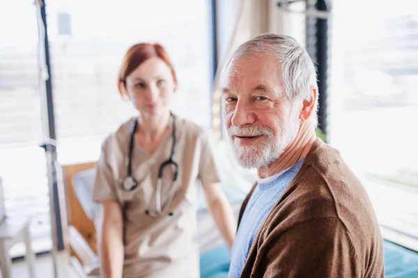 Starší pacient a lékař sedí na lůžku v nemocnici a dívají se do kamery. — Stock fotografie
