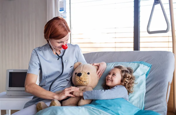 Amable médico femenino examinando niña pequeña en la cama en el hospital . — Foto de Stock