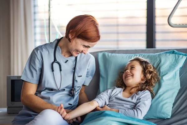 Friendly female doctor examining small girl in bed in hospital. — Stock Photo, Image