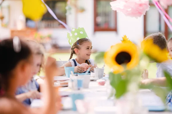 Niños pequeños sentados a la mesa al aire libre en la fiesta del jardín en verano, comiendo . — Foto de Stock