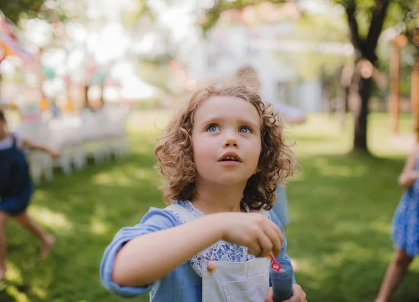 Mała dziewczynka dmuchanie pęcherzyki na zewnątrz w ogrodzie w lecie. — Zdjęcie stockowe