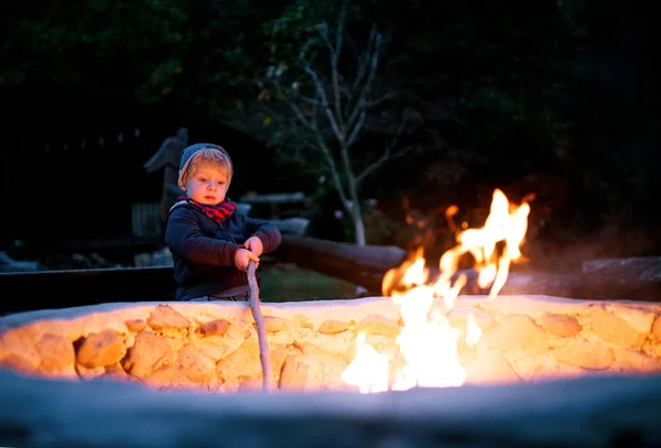 Een peuter jongen staan en spelen bij open vuur buiten in de tuin in de zomer. — Stockfoto