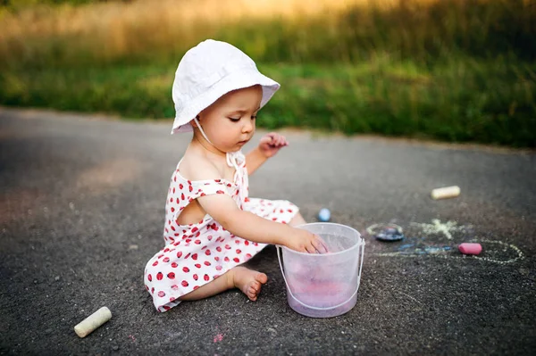 Menina bonito criança ao ar livre no campo, desenho de giz na estrada . — Fotografia de Stock