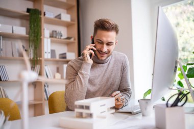 Ofisteki masada oturan genç mimar, akıllı telefon kullanıyor..