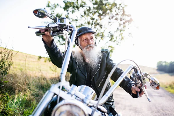 Um homem idoso viajante com moto no campo . — Fotografia de Stock