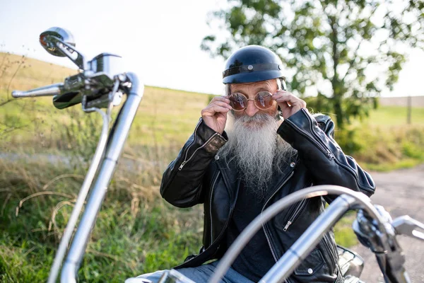 Um homem idoso viajante com moto e óculos de sol no campo . — Fotografia de Stock
