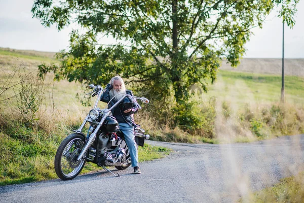 A senior man traveller with motorbike in countryside. Copy space. — Stock Photo, Image