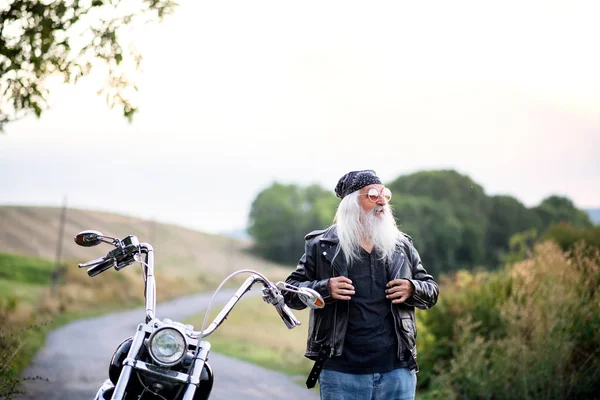 Homem idoso viajante com moto e óculos de sol no campo . — Fotografia de Stock