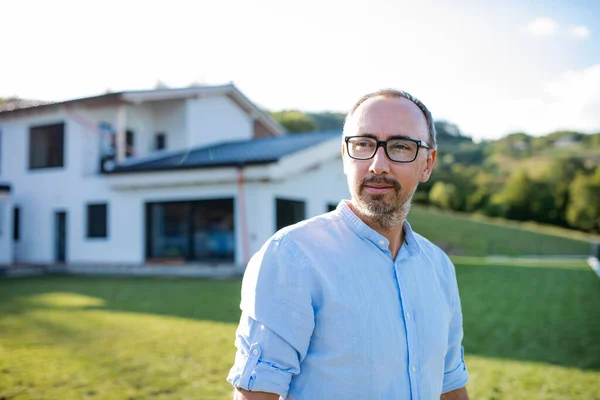 Een portret van een man die buiten in de tuin bij een huis staat. — Stockfoto