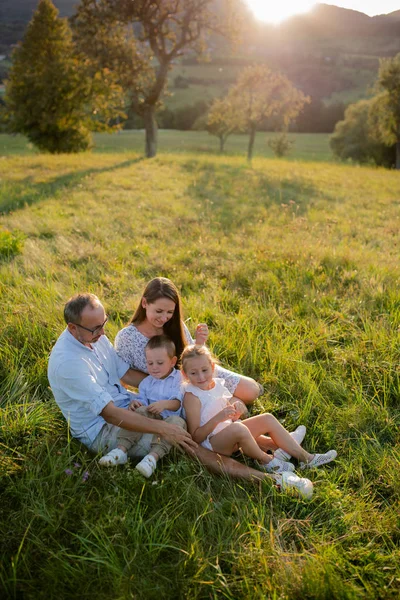 Ung familj med två små barn som sitter på äng utomhus vid solnedgången. — Stockfoto