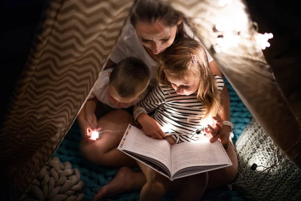 Mother with children sitting indoors in bedroom, reading a book. — 스톡 사진