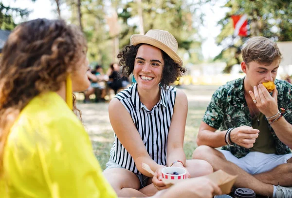 Groep jonge vrienden op het zomerfestival, zittend op de grond en etend. — Stockfoto