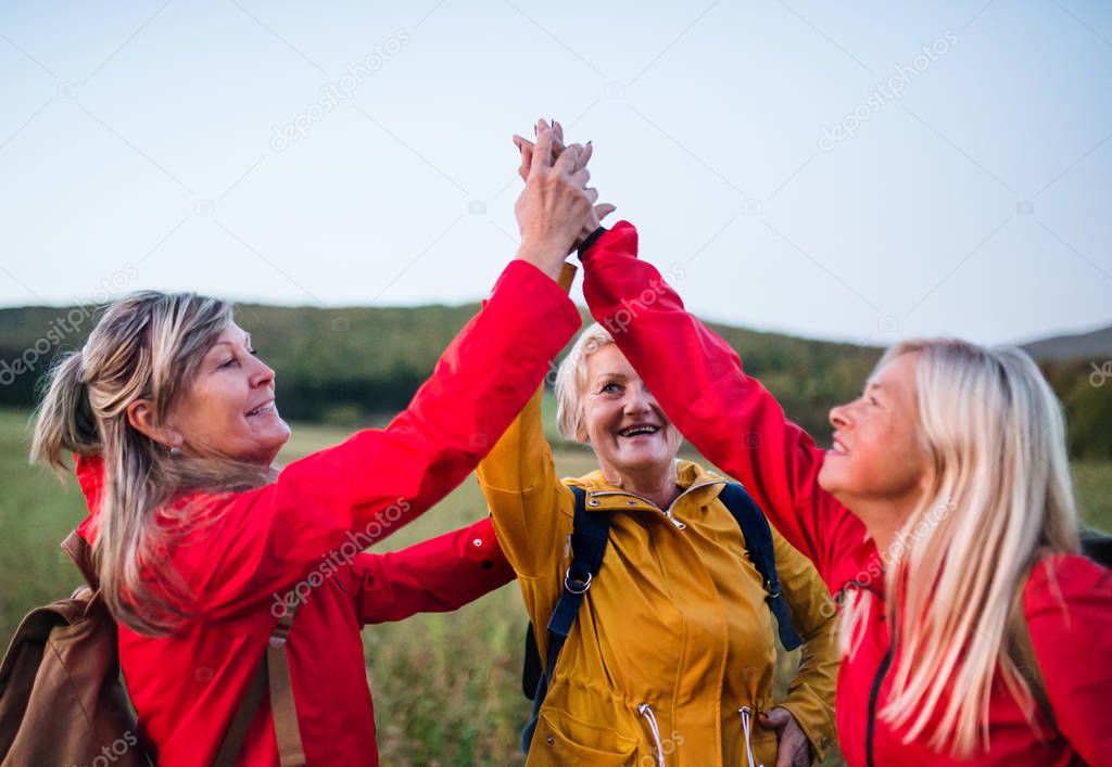 Senior women on walk outdoors in nature at dusk, giving high five.