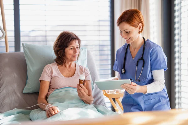 Een vrouwelijke arts met tablet die praat met een patiënt in bed in het ziekenhuis. — Stockfoto