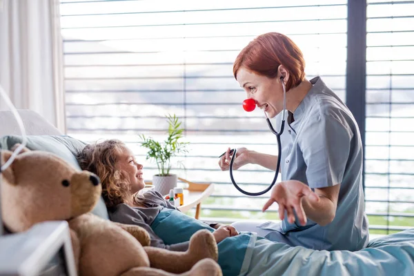 Amable médico femenino examinando niña pequeña en la cama en el hospital . —  Fotos de Stock