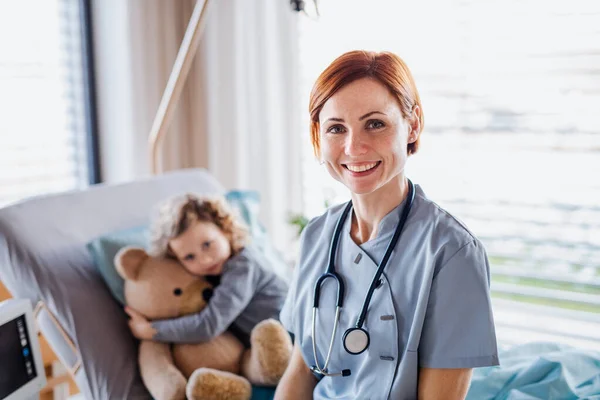 Amable médico femenino y niña pequeña en la cama en el hospital . —  Fotos de Stock