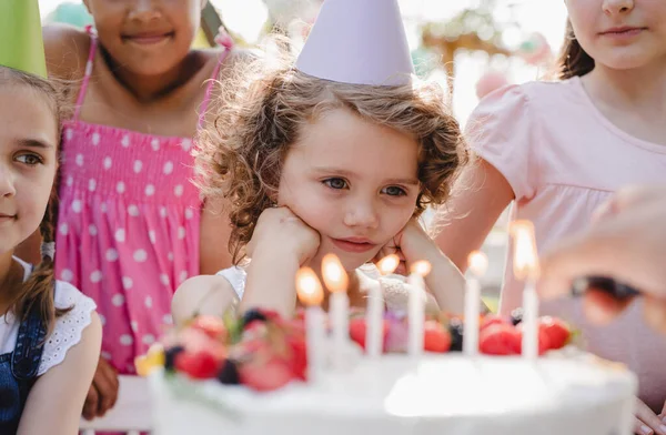 Los niños con pastel de pie alrededor de la mesa en la fiesta de cumpleaños en el jardín en verano . — Foto de Stock