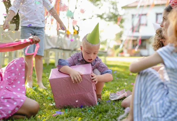 Enfant trisomique avec des amis à la fête d'anniversaire en plein air, cadeaux d'ouverture . — Photo