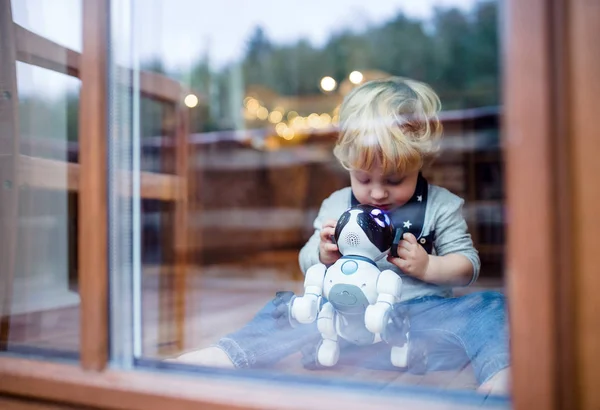 Un lindo niño sentado en casa, jugando con un perro robótico. — Foto de Stock